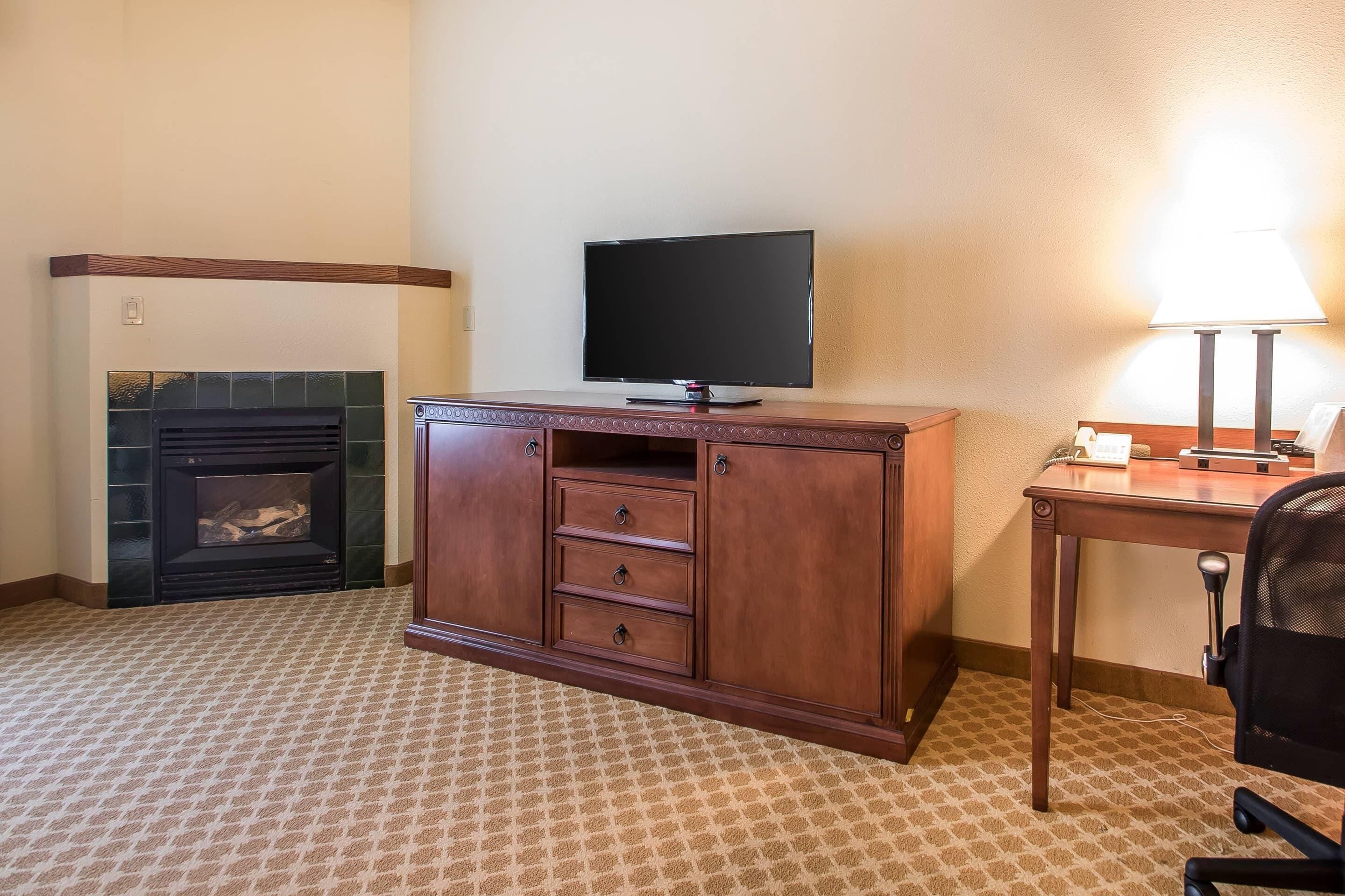 Une chambre d’hôtel avec une cheminée, un téléviseur posé sur un meuble en bois, un bureau avec une lampe et une chaise.