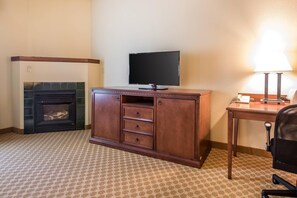 A hotel room with a fireplace, a television on a wooden cabinet, a desk with a lamp, and a chair. - Quality Inn & Suites East Troy I-43 (East Troy)