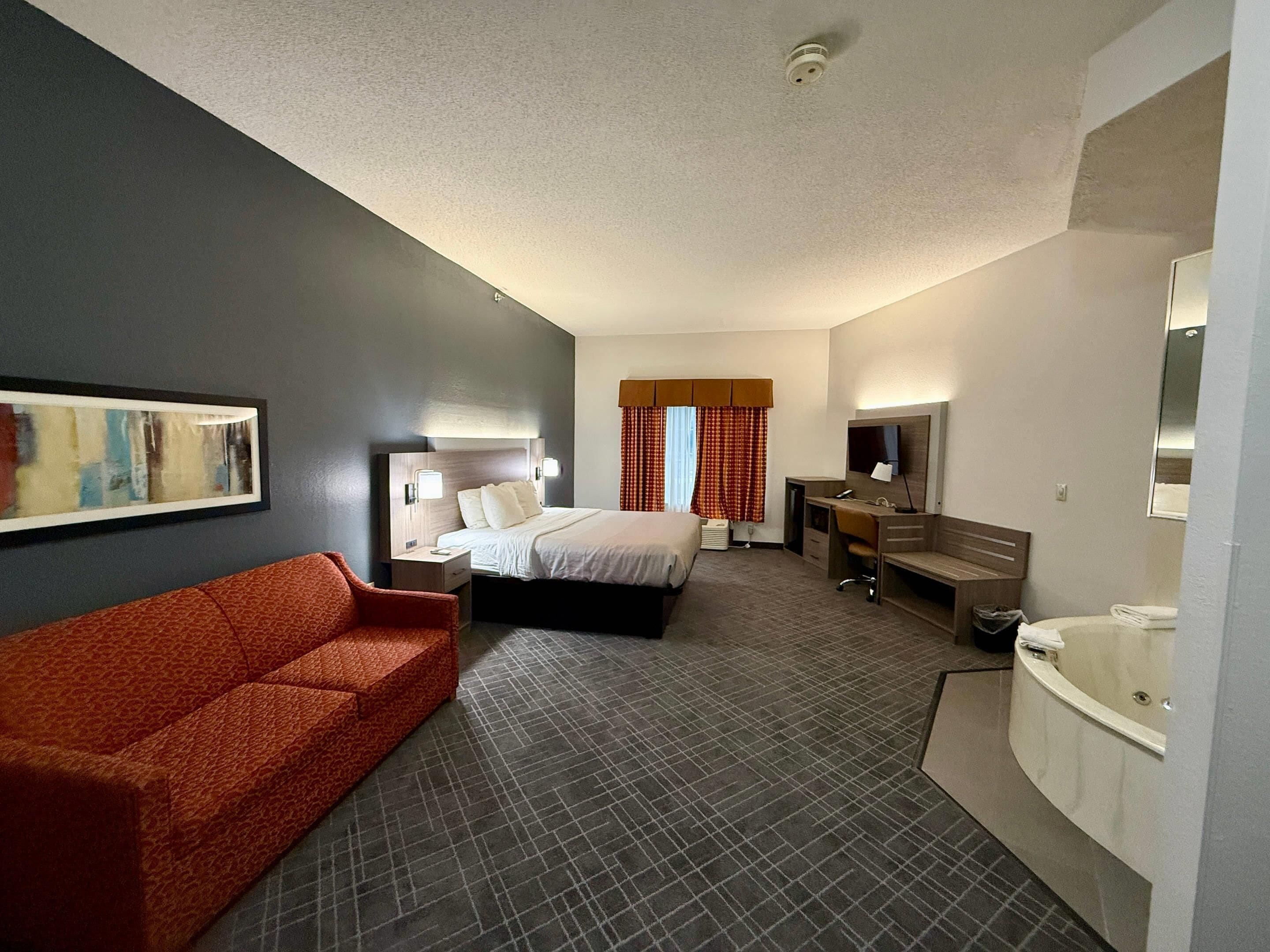 Ein Hotelzimmer mit Bett, Schreibtisch, Stuhl, Sofa, Badezimmer und einem Bild an der Wand.