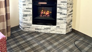A corner fireplace with a stone facade, a fire burning inside, and a striped carpet on the floor. - Quality Inn & Suites East Troy I-43 (East Troy)