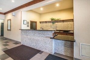 Un área de recepción con pared de piedra, mostrador de recepción, espejo y planta.
