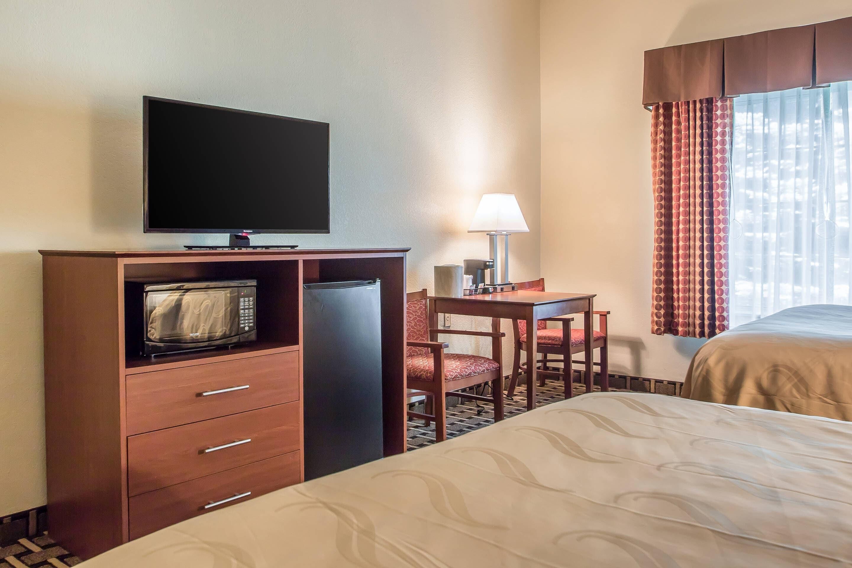 A hotel room with a bed, a desk with a lamp, a television, and a microwave.