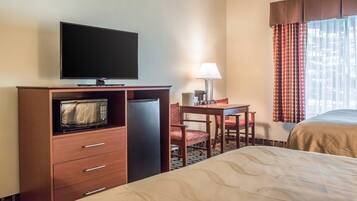 A hotel room with a bed, a desk with a lamp, a television, and a microwave.