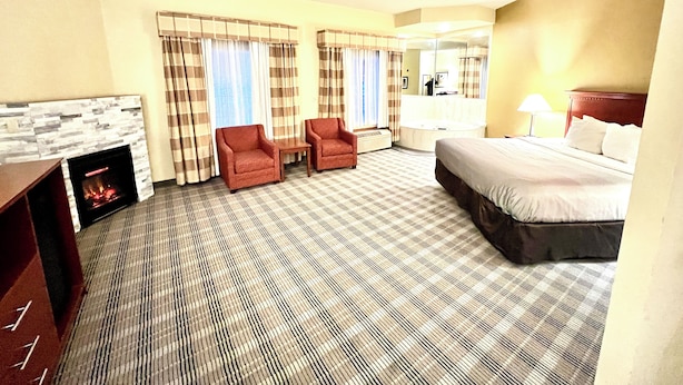 A hotel room with a bed, two armchairs, a fireplace, a large mirror, and a window with curtains. - Quality Inn & Suites East Troy I-43 (East Troy)