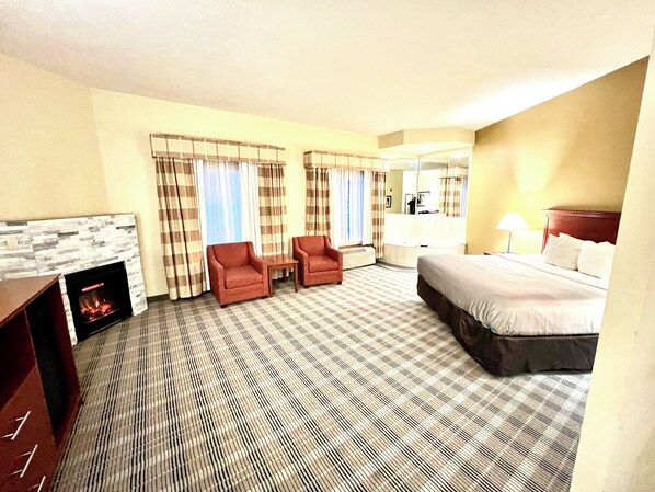 A hotel room with a bed, two armchairs, a fireplace, a large mirror, and a window with curtains.
