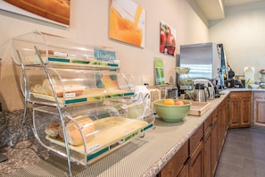 Zona de desayuno tipo buffet con mostradores que exhiben pan y bagels, un bol de fruta y una estación de café.