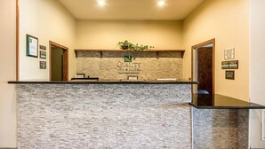A reception desk with a stone facade, a logo for Quality Inn & Suites, and a plant on top. - Quality Inn & Suites East Troy I-43 (East Troy)