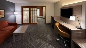 A hotel room with a bed, a desk, a chair, a TV, and a lamp.