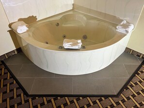 A corner bathtub with a white marble finish, a small control panel, and two towels.
