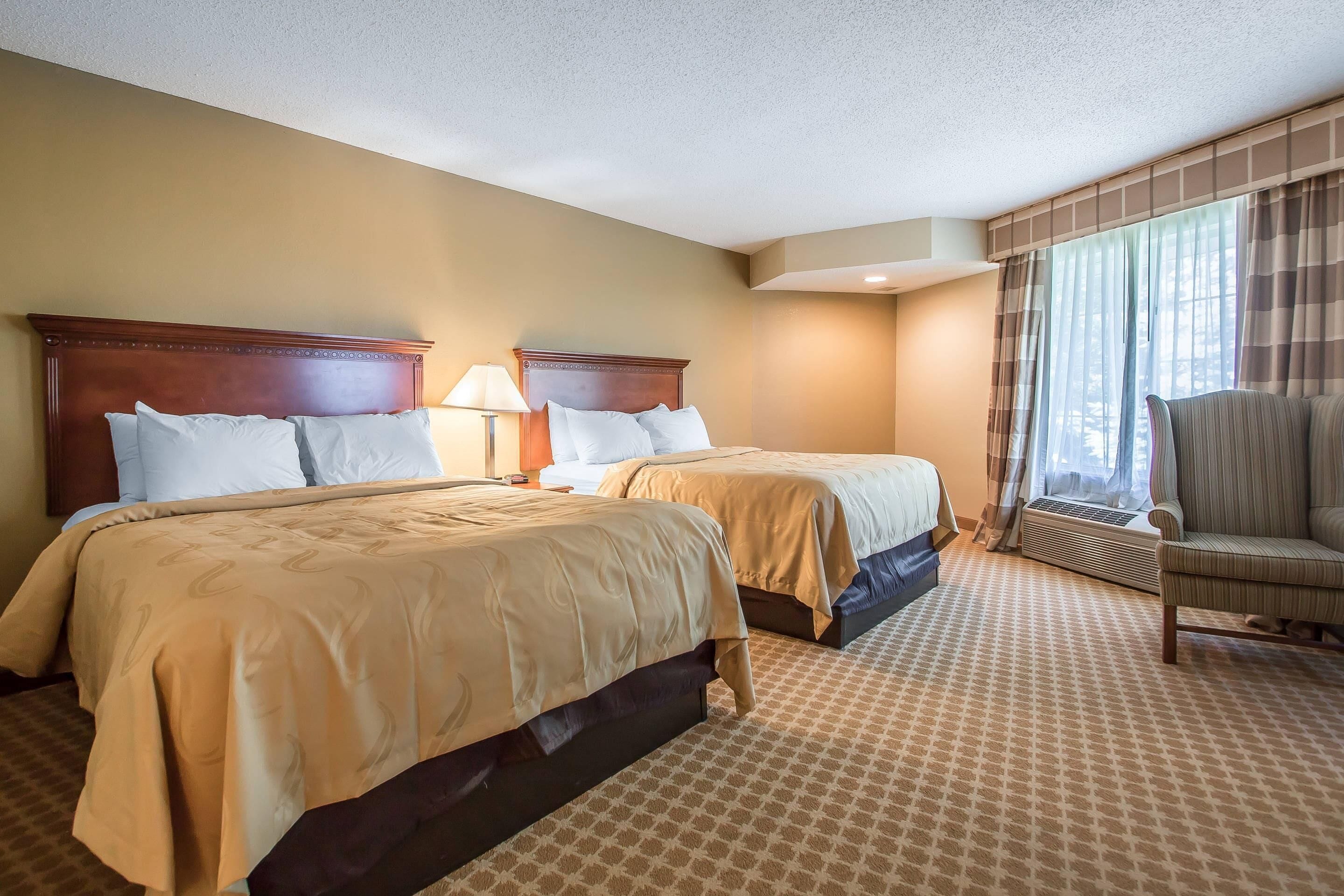 A hotel room with two beds, a chair, and a window with curtains.