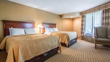 A hotel room with two beds, a chair, and a window with curtains.