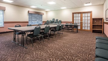 Ein Konferenzraum mit großem Tisch, mehreren Stühlen, einer Projektionsleinwand und einer Tür mit Glasverkleidung.
