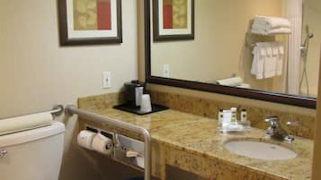 A bathroom with a toilet, sink, and mirror. There are framed pictures on the wall, a blue trash bin, and a towel rack with towels.