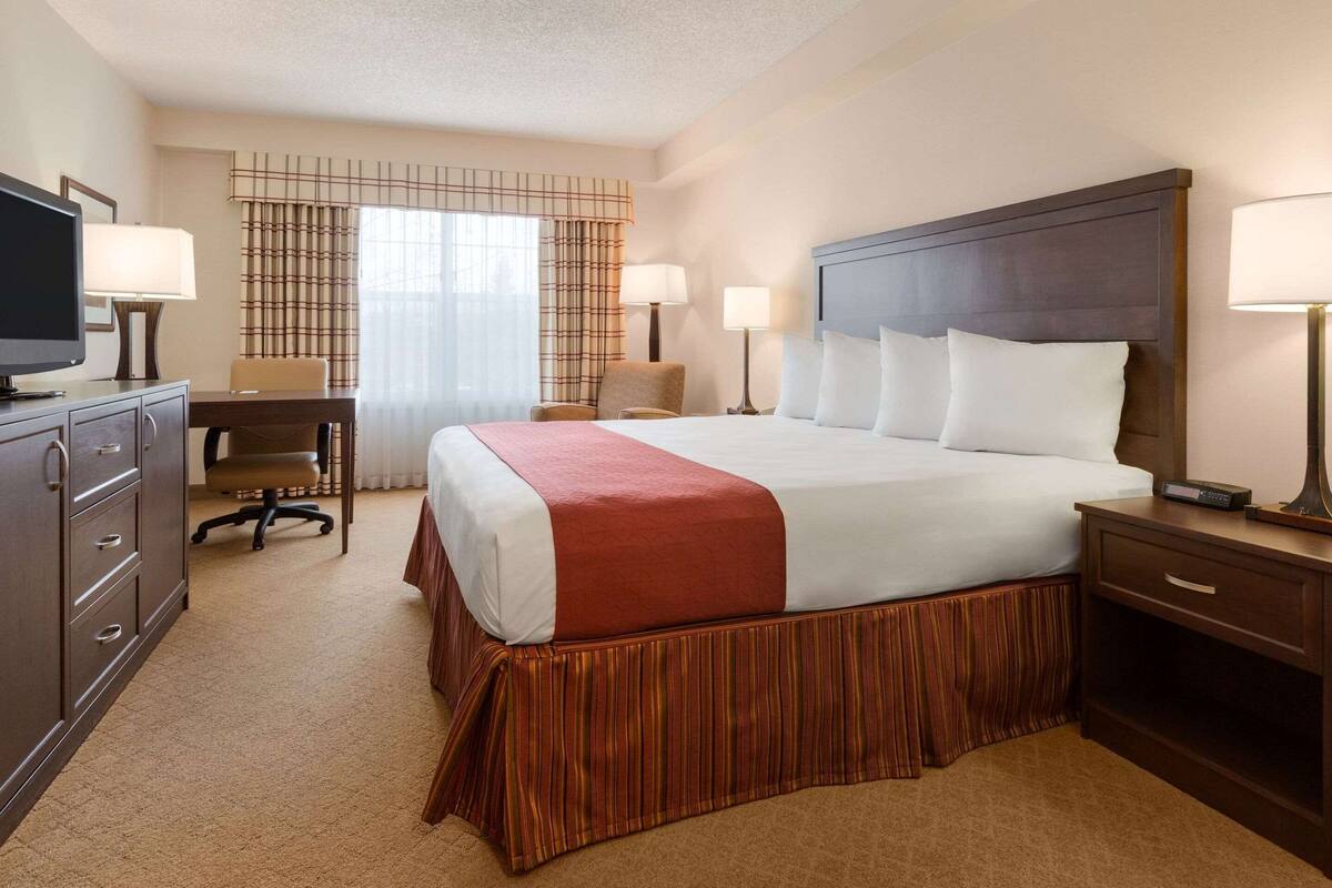 A hotel room with a large bed, a desk, a chair, a TV, and two bedside lamps.