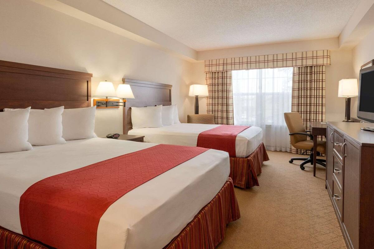 A hotel room with two beds, a desk, a chair, and a television.