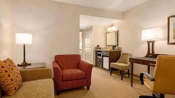 A hotel room with a sofa, armchair, desk, and kitchenette.