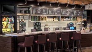A bar area with a counter, bar stools, a menu board, and a variety of bottles and glasses.