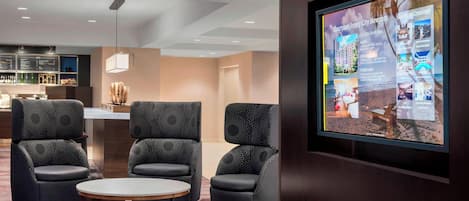 Un vestíbulo de hotel moderno con una pantalla grande que muestra los servicios del hotel y una zona de bar con su menú.