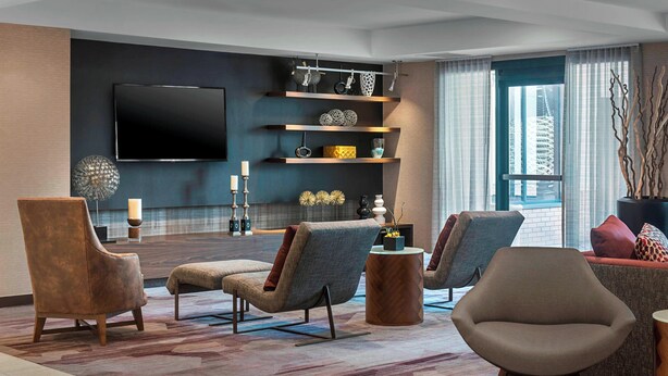 A modern living room with a flat-screen TV, comfortable seating, decorative shelves, and a view of the city.