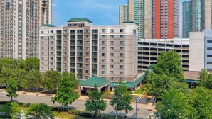 A Courtyard hotel with a green roof, surrounded by tall buildings and trees.
