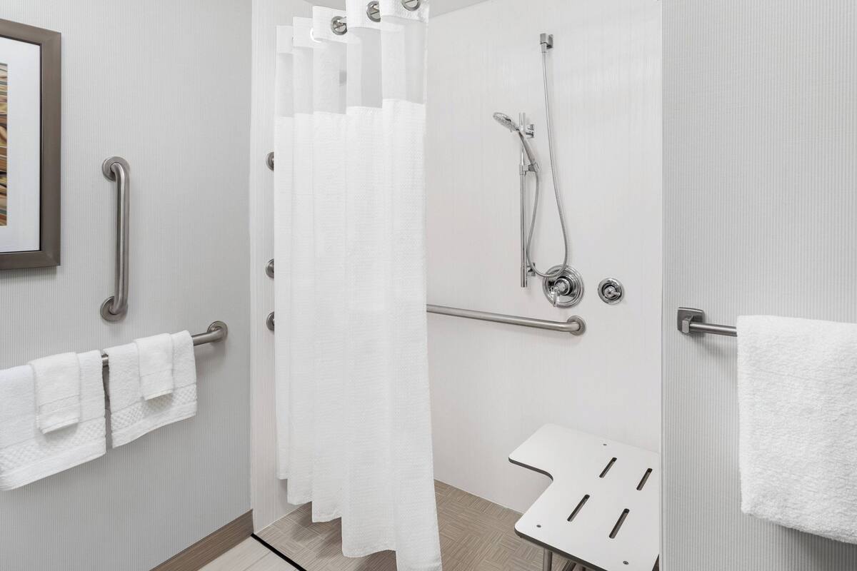 Une salle de bain moderne équipée d’une douche, de barres d’appui et d’un porte-serviettes blanc.