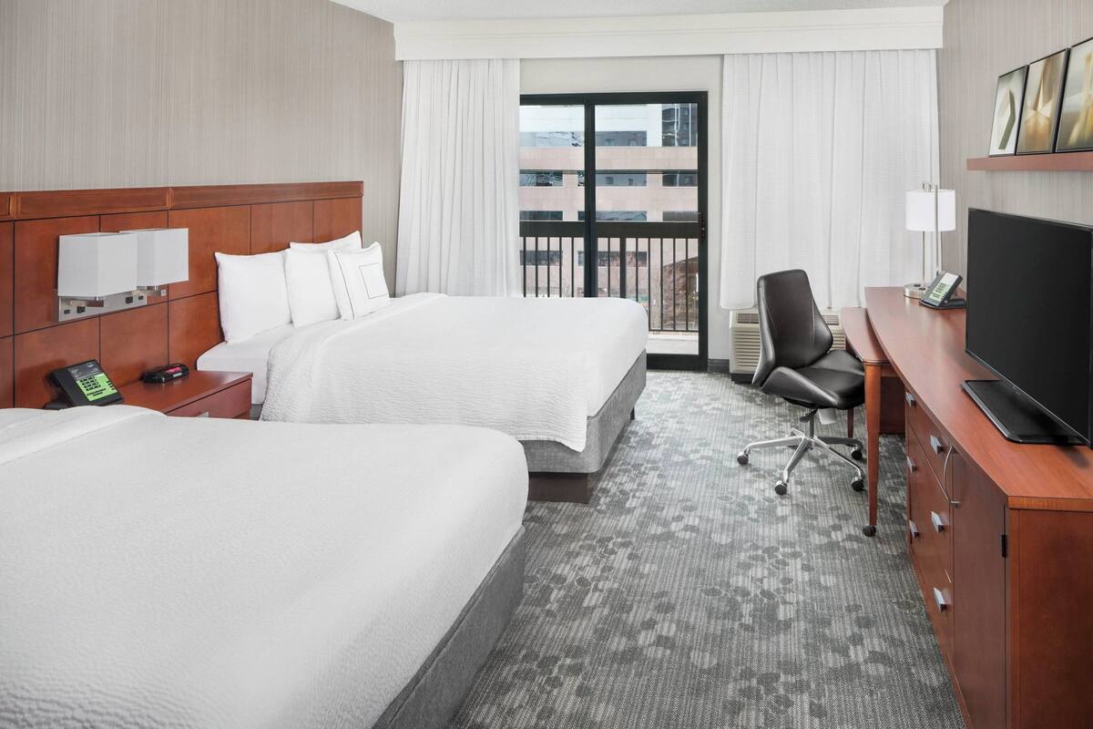 Une chambre d’hôtel avec deux lits, un bureau avec une télévision, une chaise et un téléphone sur la table de chevet.
