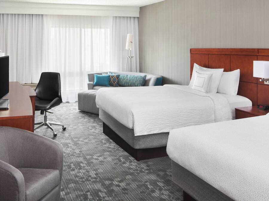 A hotel room with a large bed, a desk with a computer, a chair, and a TV.