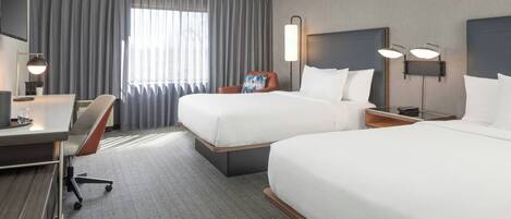 A hotel room with two beds, a desk, a chair, and a large window with curtains.