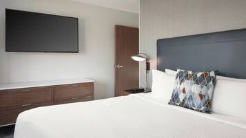 Une chambre d’hôtel dotée d’un grand lit, d’un téléviseur à écran plat fixé au mur, d’une armoire en bois et d’une table de chevet avec une lampe.