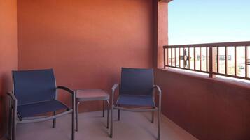 A balcony with two chairs and a small table, a red wall, and a view of the street.