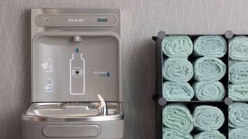 Ein Wasserspender mit digitaler Anzeige und einem Flassymbol neben einem Ordner ordentlich gerollter Handtücher.