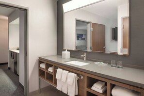 A modern bathroom with a large mirror, a sink, and a vanity with shelves for towels. - Courtyard by Marriott Farmington (Farmington)