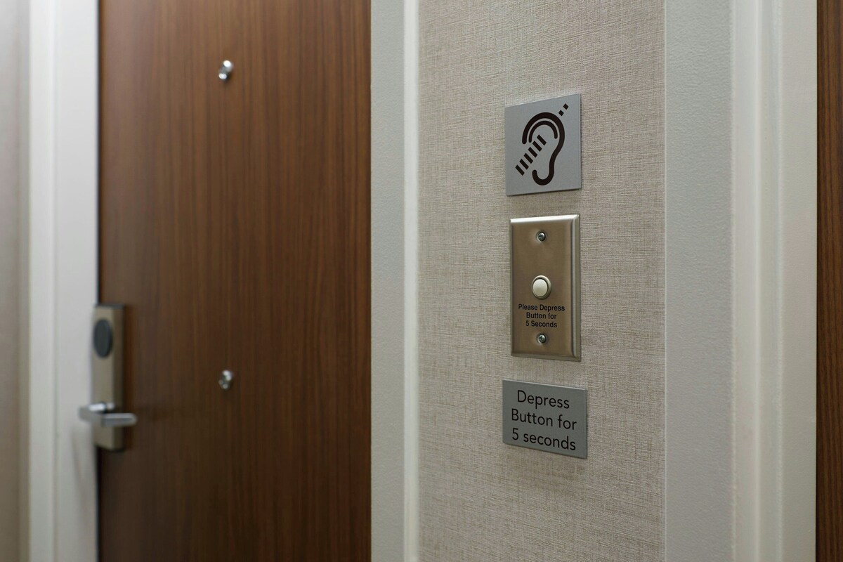 A door with a button for the deaf and hearing impaired, and a sign instructing to depress the button for 5 seconds.