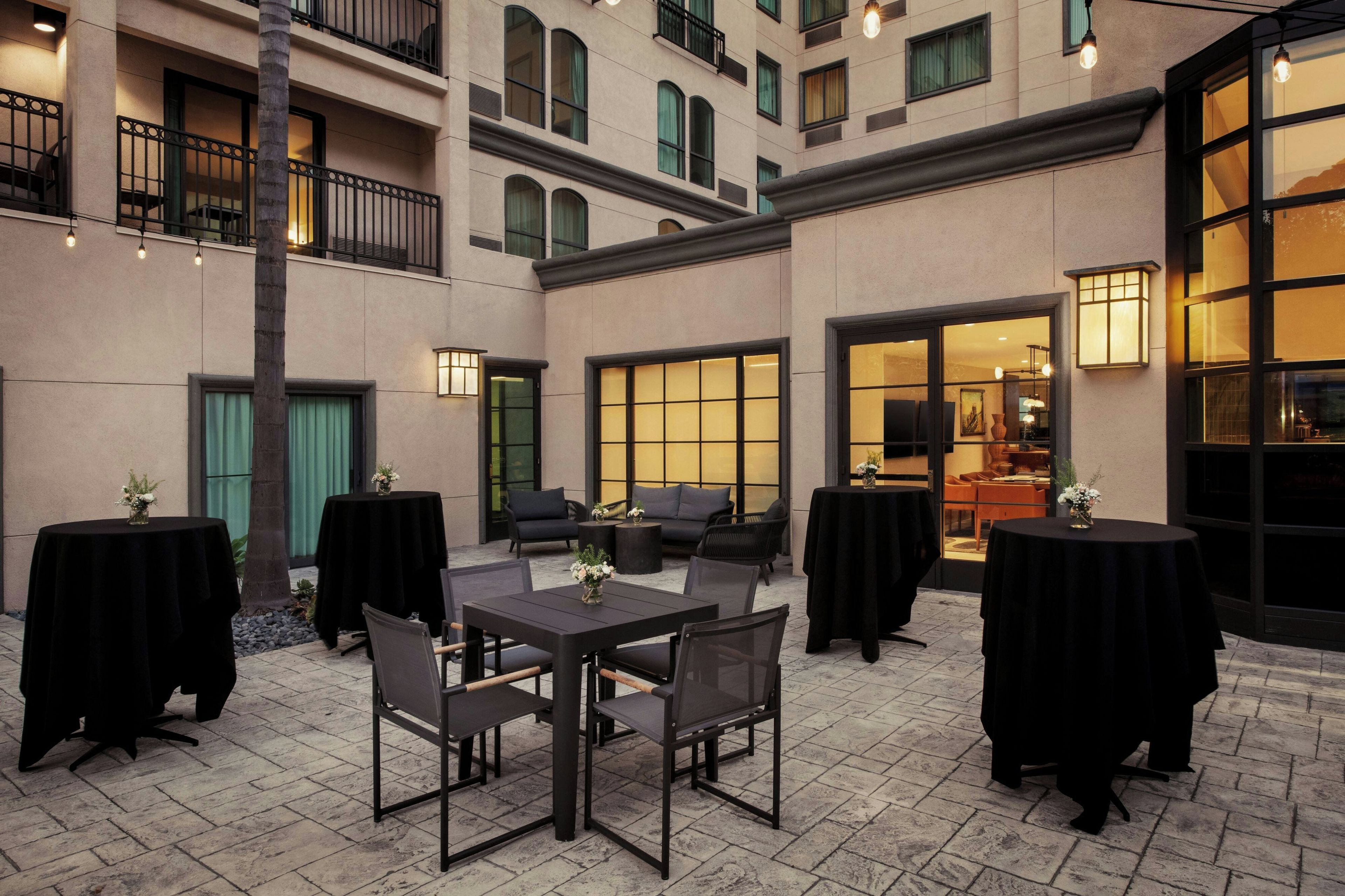 An outdoor patio area with tables and chairs, a building entrance, and a view into the interior.