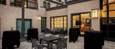 An outdoor patio area with tables and chairs, a building entrance, and a view into the interior.