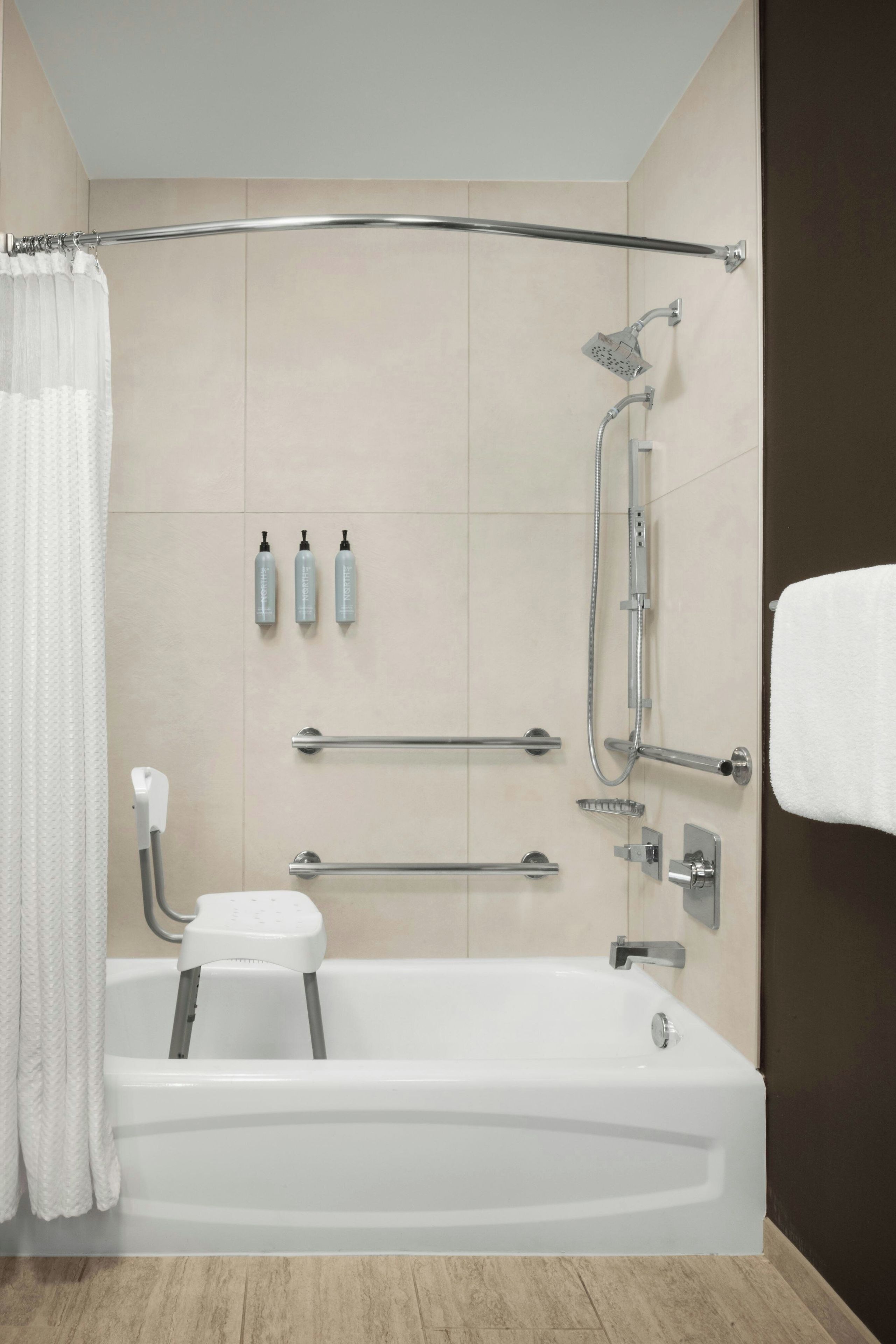 A modern bathroom with a bathtub, shower, grab bars, and a toilet.