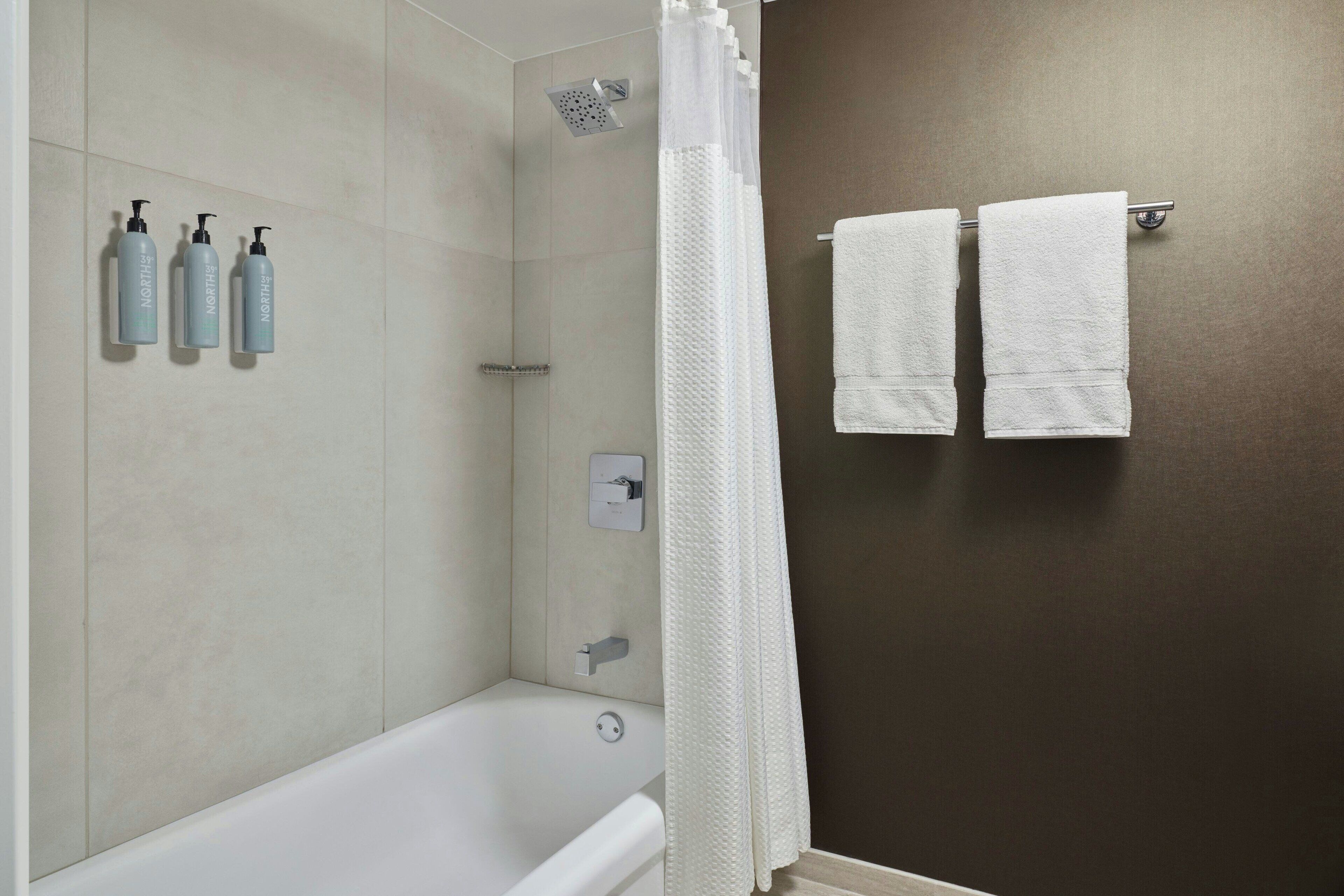 Un baño moderno con bañera, ducha y tres botellas de champú en la pared.