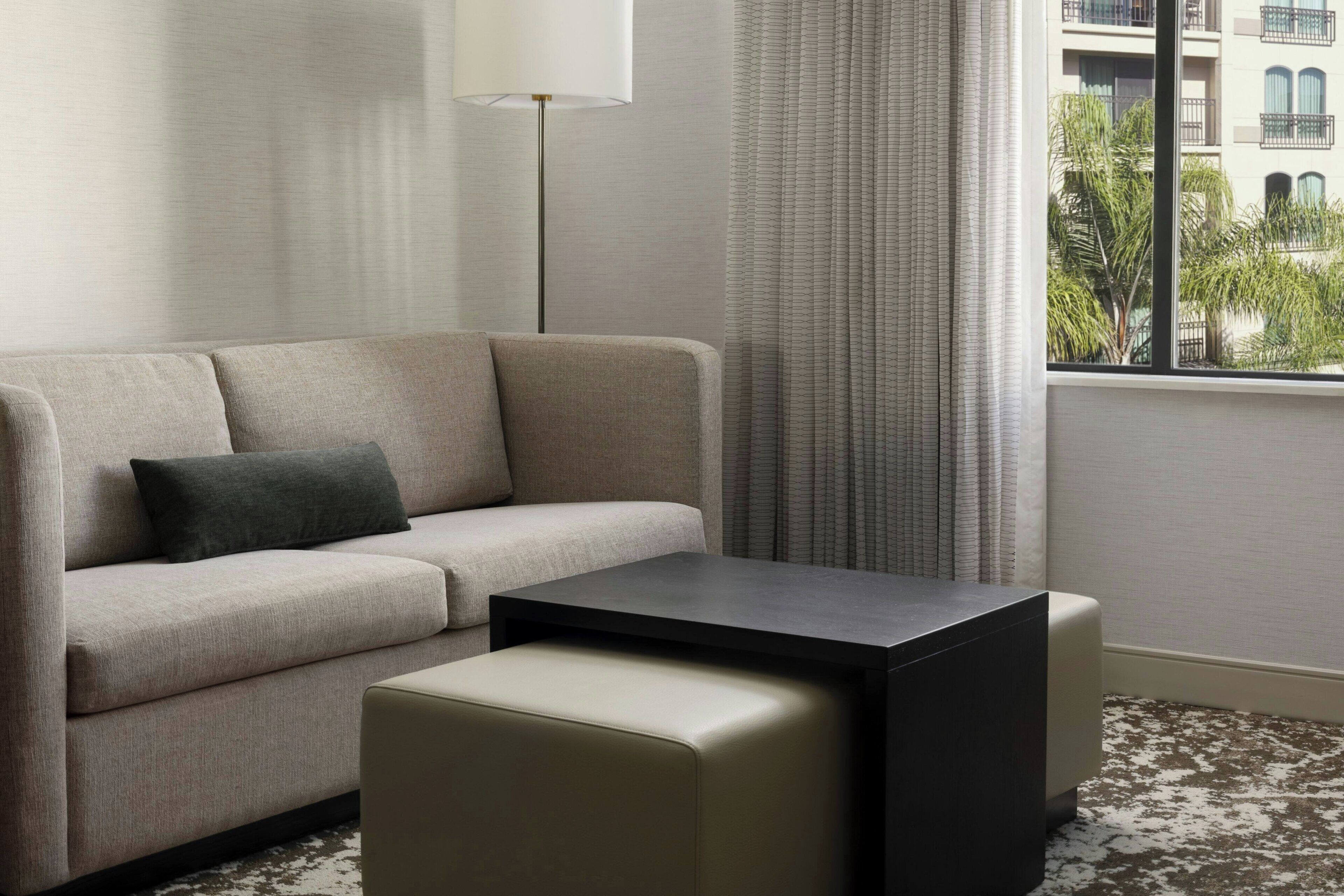 A modern living room with a sofa, a coffee table, and a view of a building through a window.