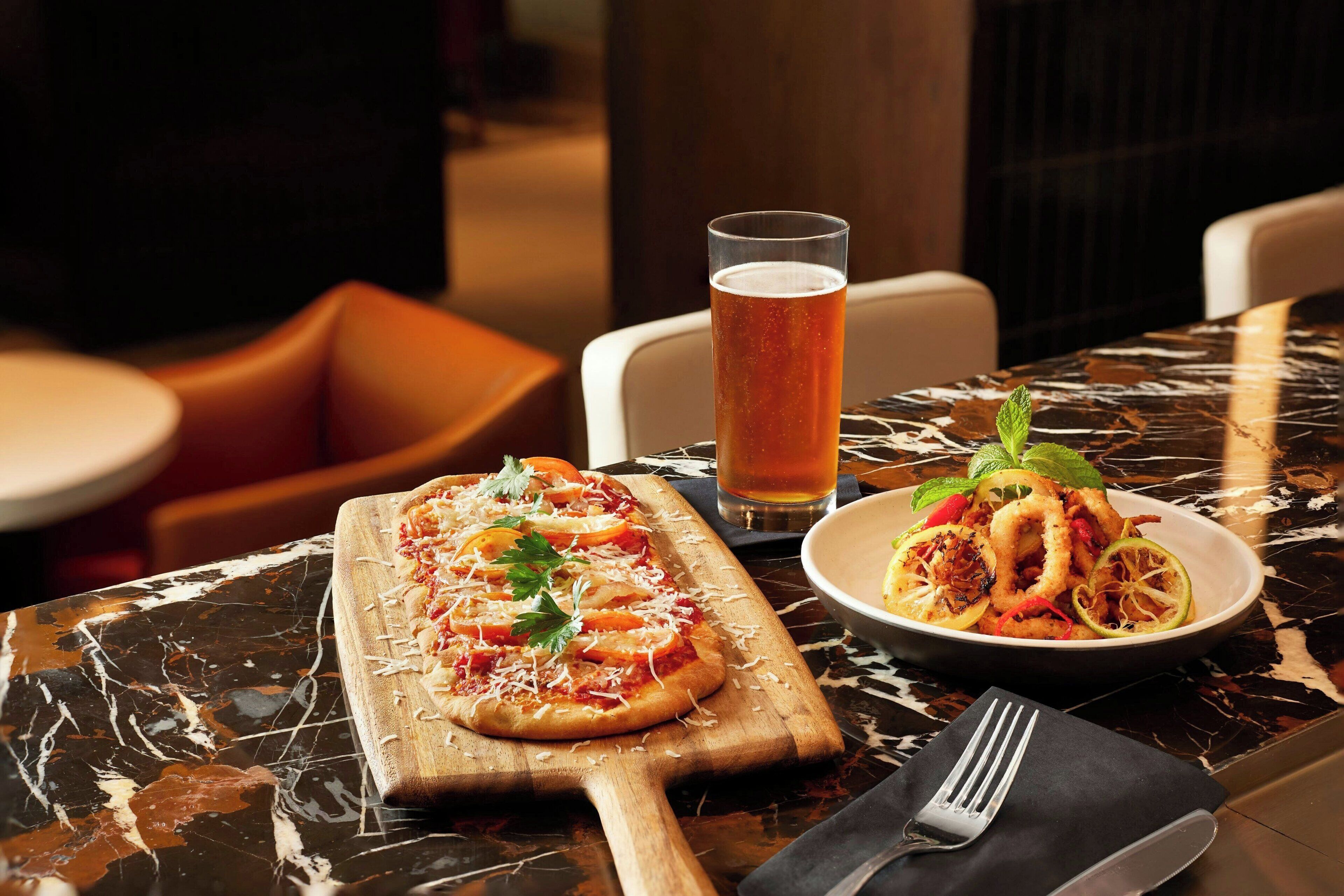 Una mesa de comedor con pizza, mariscos en un plato y una cerveza en un vaso.