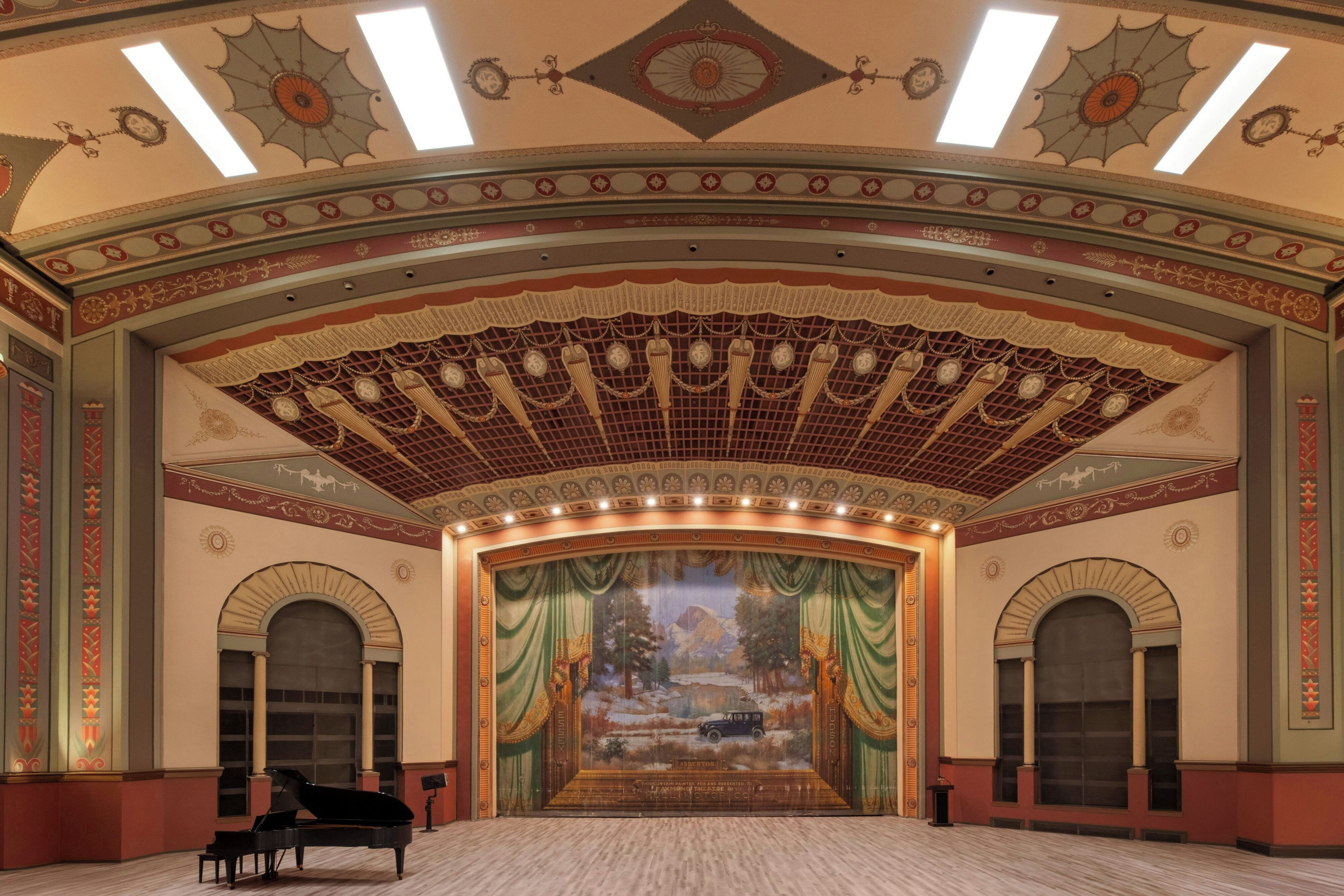A grand theater with a large stage, arched windows, and a grand piano.