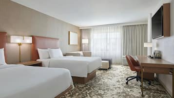 A hotel room with two beds, a desk, a chair, a TV, and a large window with curtains.