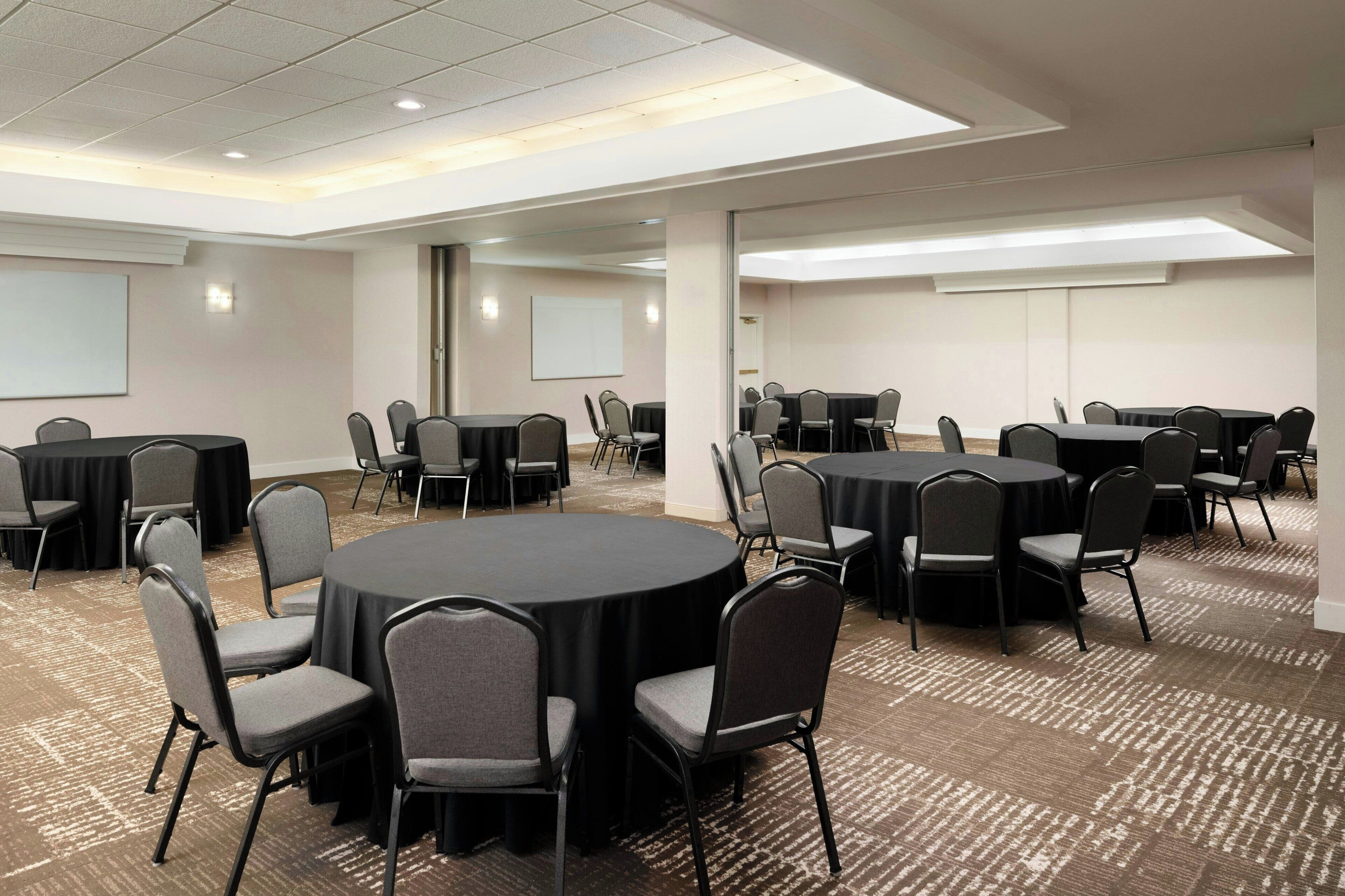 A conference room with multiple round tables and chairs, carpeted flooring, and a whiteboard on the wall.