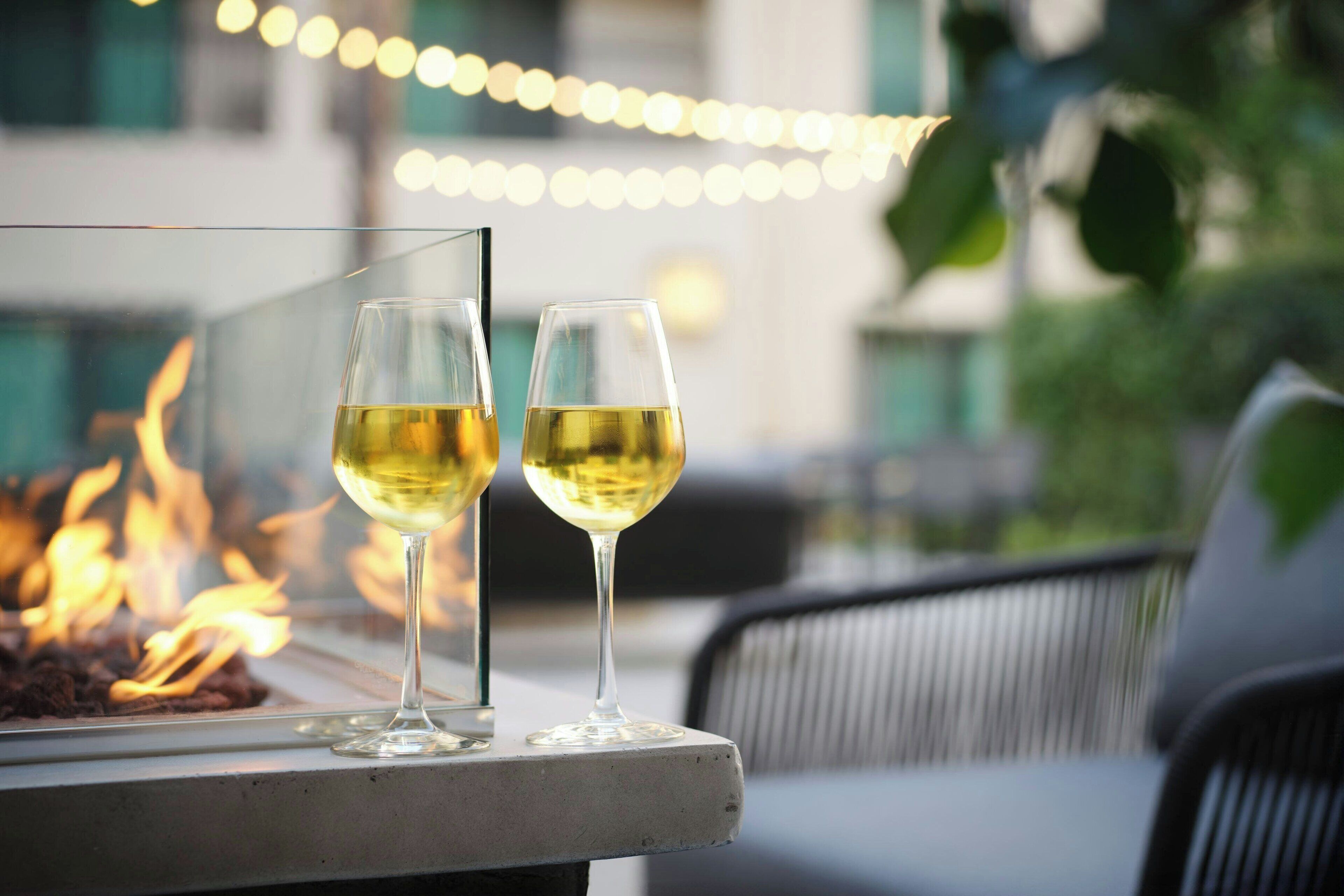 Two glasses of white wine on a table with a fire in the background.