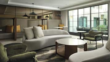 Una sala de estar moderna con un sofá, sillones y una mesa de centro. Amplias ventanas ofrecen luz natural y vistas al exterior.