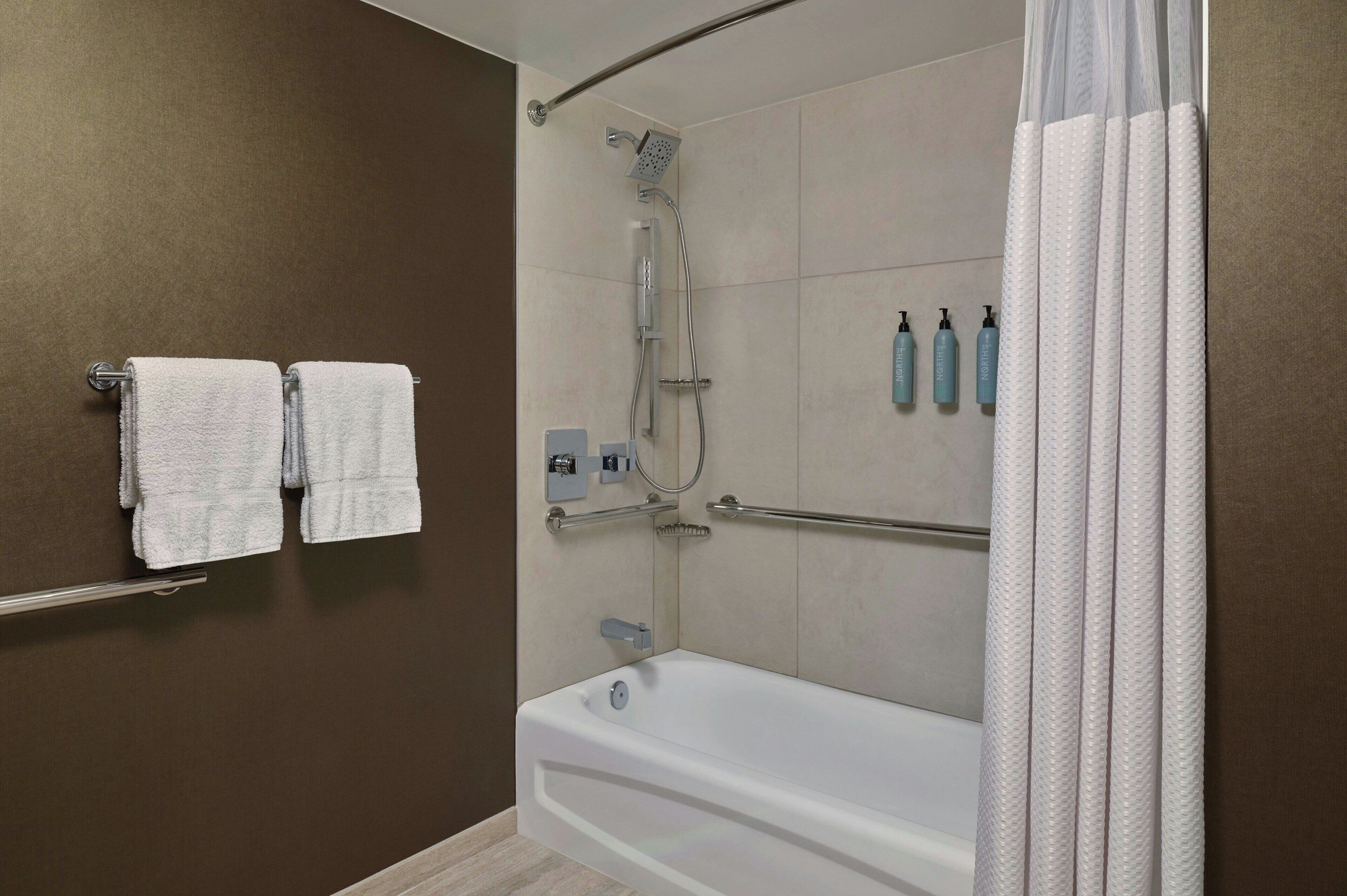 A modern bathroom with a bathtub, shower, and two towels hanging on a rack.