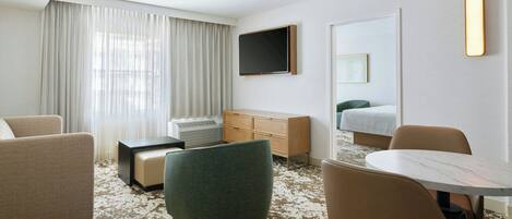 Una habitación de hotel con una cama grande, un escritorio, una silla, un sofá y un televisor montado en la pared.