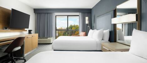 Une chambre d’hôtel équipée d’un lit, d’un bureau, d’une chaise, d’une télévision et d’un balcon avec vue.