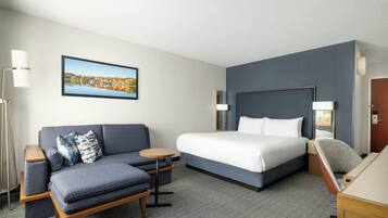 A hotel room with a bed, a sofa, a desk, and a chair.