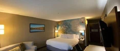 A hotel room with a bed, a sofa, a desk, and a painting on the wall.