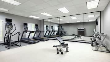 A gym with treadmills, elliptical machines, a bench press, and dumbbells.